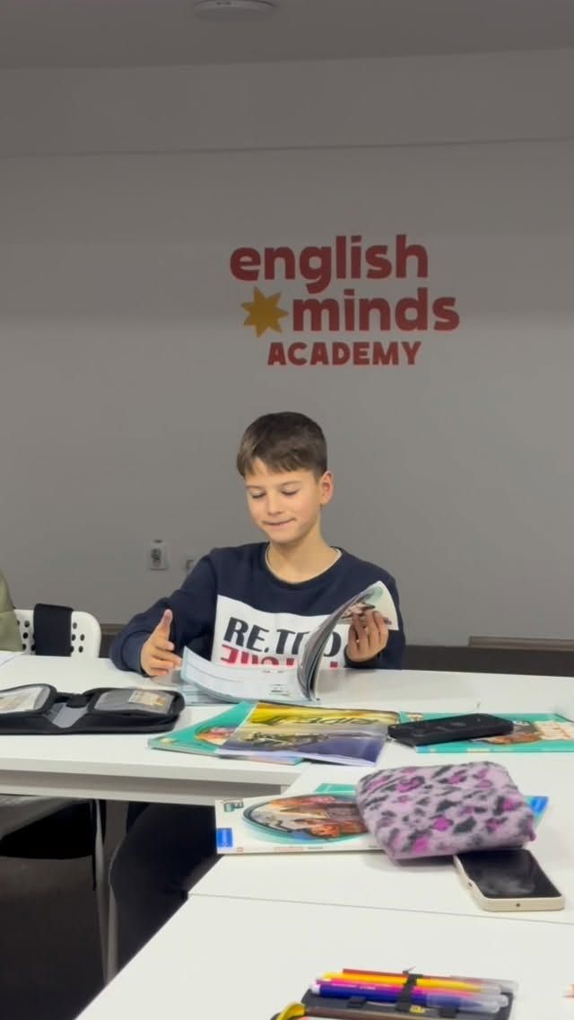 Un băiat răsfoiește un manual de engleză la o masă din sala de curs.