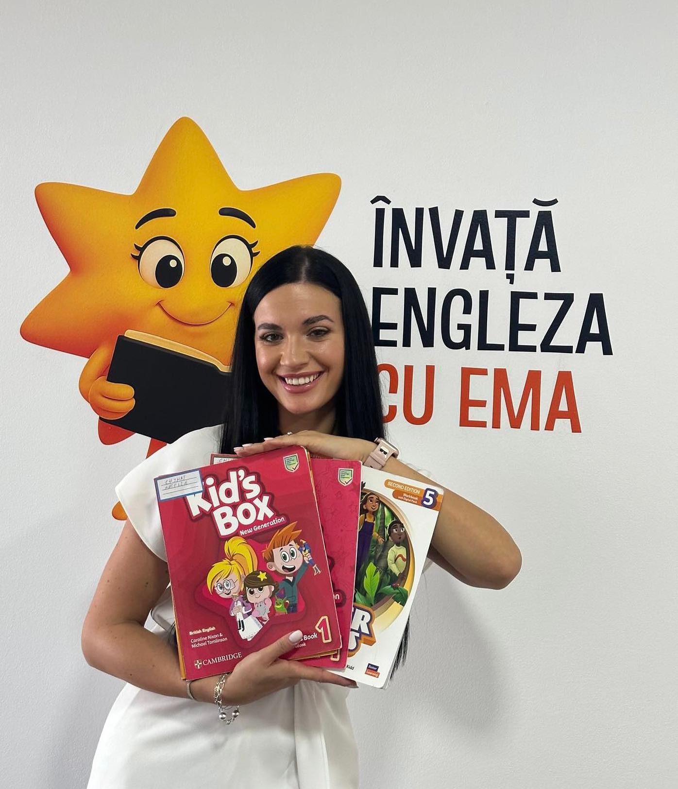 Profesoara Ema ține în brațe manuale Cambridge, în fața mascotei stelei de pe peretele sălii.